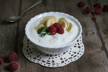 Natural homemade yoghurt in a bowl with banana slices and raspberries. Healthy breakfast with Greek yogurt