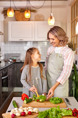 family mother with daughter cooking together, happy girl is glad to help mother preparing salad,...