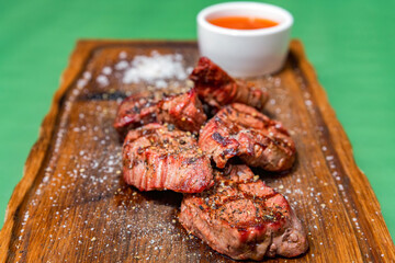 Grilled beef medallions served on a wooden kitchen board garnished with sauce