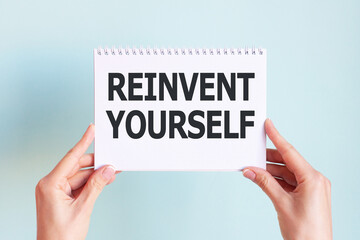 REINVENT YOURSELF word inscription on white card paper sheet in hands of a businesswoman. recap concept