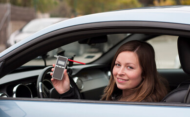 Fototapeta na wymiar drink and drive young female driver being subject to test for alcohol content with use of breathalyzer. she is smiling as she does not drive and drink