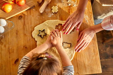 Obraz na płótnie Canvas mother teaching daughter how to make cookies from dough using cookie cutters. top view