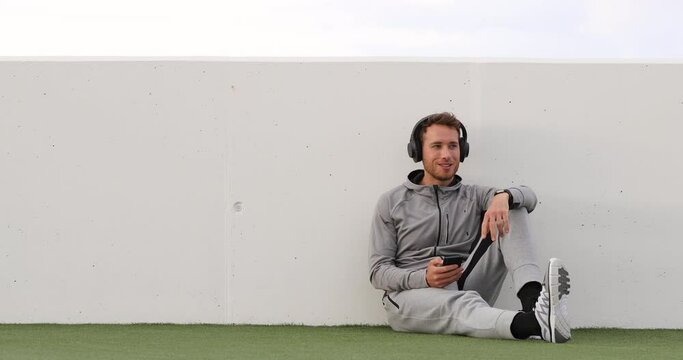 Podcasts - Man listening to music mobile phone podcast app wearing headphones sitting outdoors on grass. Healthy lifestyle sport athlete using smartphone on break outdoors. Slow motion 59.94 FPS.