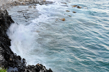 Turquoise waves breaking against a rocky and stony beachfront. South Tyrrhenian Sea.