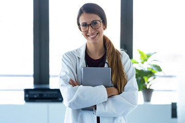 Happy young female doctor smiling and looking at camera while digital tablet and standing in the consultation.