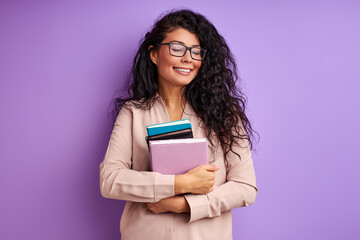 female teacher with books in hands isolated on purple background, young lady in eyeglasses enjoy education, laugh