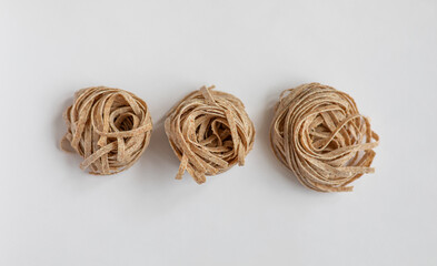 Raw whole grain brown pasta on a white background. Delicate wholemeal pasta made of graham flour, rich in nutrients protein, carbohydrates and fiber