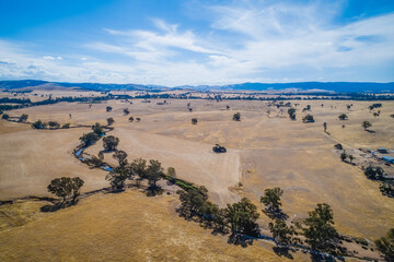 Fototapeta na wymiar Small creek passing through agricultural land with hills on the horizon in Australia - aerial view