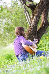 Blonde attractive teenager girl playing guitar in spring garden.