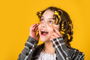 Happy child with eye patches. Hairdresser salon. Girl with curlers and hair clips in her hair on yellow background. Little girl curlers around her hair. Create beautiful hairstyle. Gorgeous hairstyle