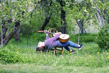 Blonde happy attractive teenager girl with the guitar in spring garden