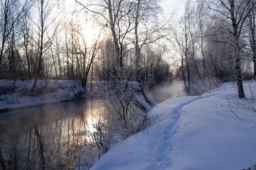 View of the snow-covered bank of the Pekhorka River in the rays of the setting sun.