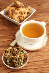 Oatmeal cookies with walnuts and raisins, sugar-coated pumpkin seeds cookies in a bowls and a cup of green tea on a wooden table. Closeup
