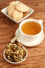 Almond cookies and sugar-coated pumpkin seeds cookies in a bowls and a cup of green tea on a wooden table. Closeup