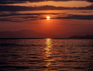 orange fiery sundown sky with some clouds over calm sea, romantic nature background.