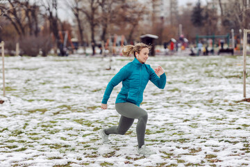 Fototapeta na wymiar Sportswoman doing lunges in park on snowy weather. Winter fitness, cold weather, park, snow