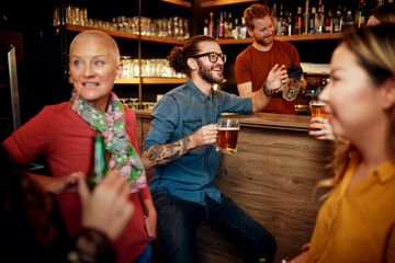 Group of cheerful friends standing near bar counter, drinking beer and chatting.