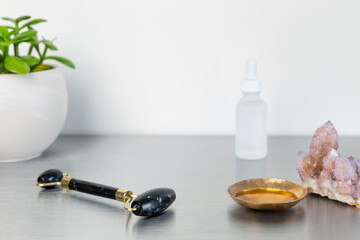 Wellness self care flat lay with obsidian jade roller, oil serum, quartz crystal, succulent plant, and white glass eye dropper