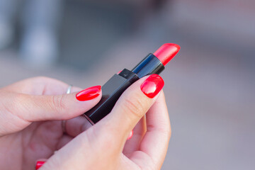 Beautiful female hands with red manicure nails and rings, holding lipstick