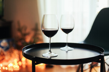 Two glasses of red wine on a table, cosy room with candid lights, chairs, carpet and a tv
