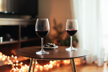 Two glasses of red wine and olives on a table, cosy room with candid lights, concept of romantic evening