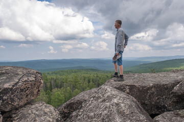 Obraz premium A middle-aged man at the top of the mountain enjoys a stunning view of the hilly valley. Freedom and goal achievement.