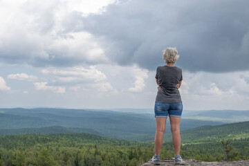 A middle-aged woman at the top of the mountain enjoys a stunning view of the hilly valley. Healthy lifestyle. Copy space