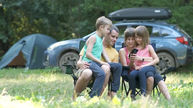 Happy young family sitting together at campsite and taking selfie with mobile phone.