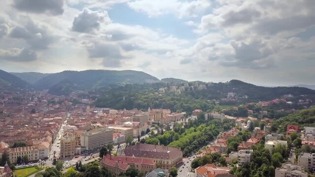 Aerial view of Brasov city, medieval town situated in Transylvania, Romania. Old architecture surrounded with big Carpathian mountains covered with dense green forest.