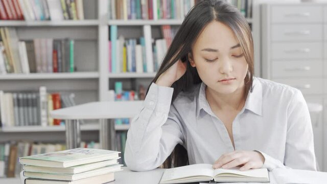 Asian young woman falling asleep while studying at the library. Lovely female student feeling sleepy and tired, preparing for exams at local library. Overworking concept