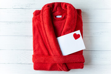 
A red bathrobe and a letter decorated with a heart are on a light wooden background. Message for...