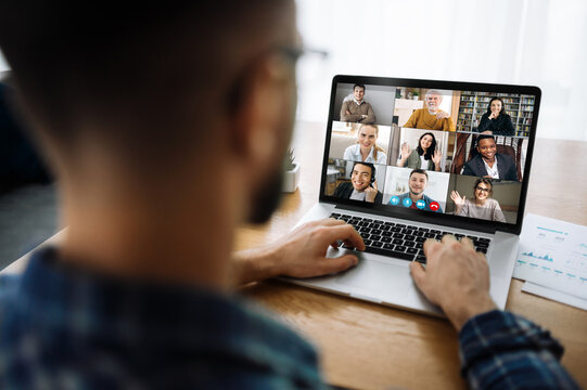 Over shoulder view to a laptop screen with many multiracial successful employees, coworkers communicating by video call, online meeting concept. Video conference with many people together