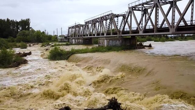 Railway metal bridge over dirty river with muddy water in flooding period during heavy rains in spring.