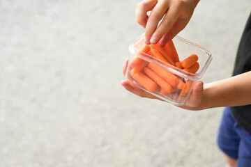 Baby carrots snack container in kid's hand with empty space for text and grey background.. Healthy snack for children concept. 