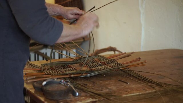 A basketmaker shapes and weaves together the wooden rods while making a traditional welsh basket by hand.