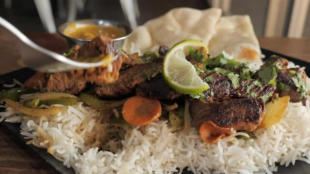 Sauced fork picks up piece of beef from plated tandoori kabob dish, slow motion slider close up 4K