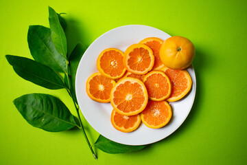 cut oranges on a white plate with green background