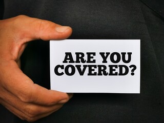 Hand holding white card with text ARE YOU COVERED.Business insurance concept.