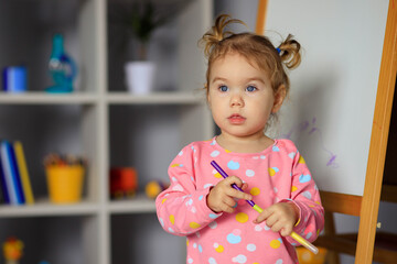 Happy cute little girl draws on a white board with a felt-tip pen.