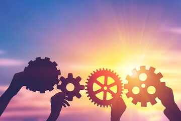 Silhouette hands holding gear from at sunlight background. concept of a teamwork cooperation idea.
