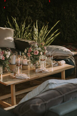 wooden table with candles and colorful flowers, armchairs with cushions on a natural plant background.