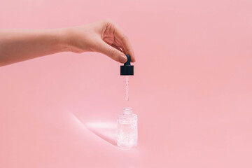 Liquid skincare serum Photo in minimal style Girl is holding pipette with cosmetic product on pink...