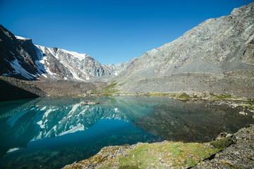 Fototapeta na wymiar Snowy mountain reflected in clear water of glacial lake. Beautiful sunny landscape with glacier reflection in water surface of mountain lake under clear sky. Snow on rock reflected in mountain lake.