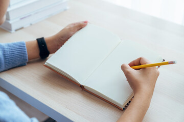 Woman holding pen and write in book on the table.