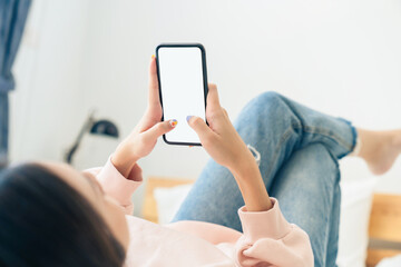 Young Asian woman sitting on the bed and holding a smartphone and using internet online.