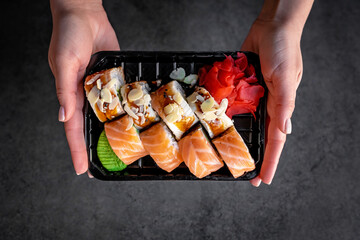 Closeup sushi in box food delivery online service. Girl holds Japanese rolls with salmon and avocado in hands