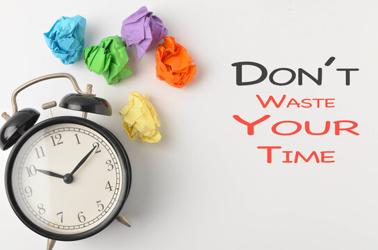 Dont Waste Your time written with alarm clock and paper trash on white background.