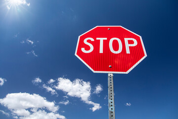 Bright red new stop sign isolated against blue sky and clouds