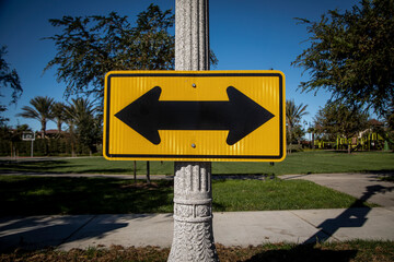 Yellow Road sign on a street pole with arrows pointed in opposite directions facing east and west...