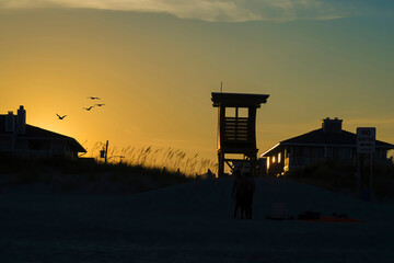 Silhouette of a lifeguard tower with seagulls flying on the yellow horizon.